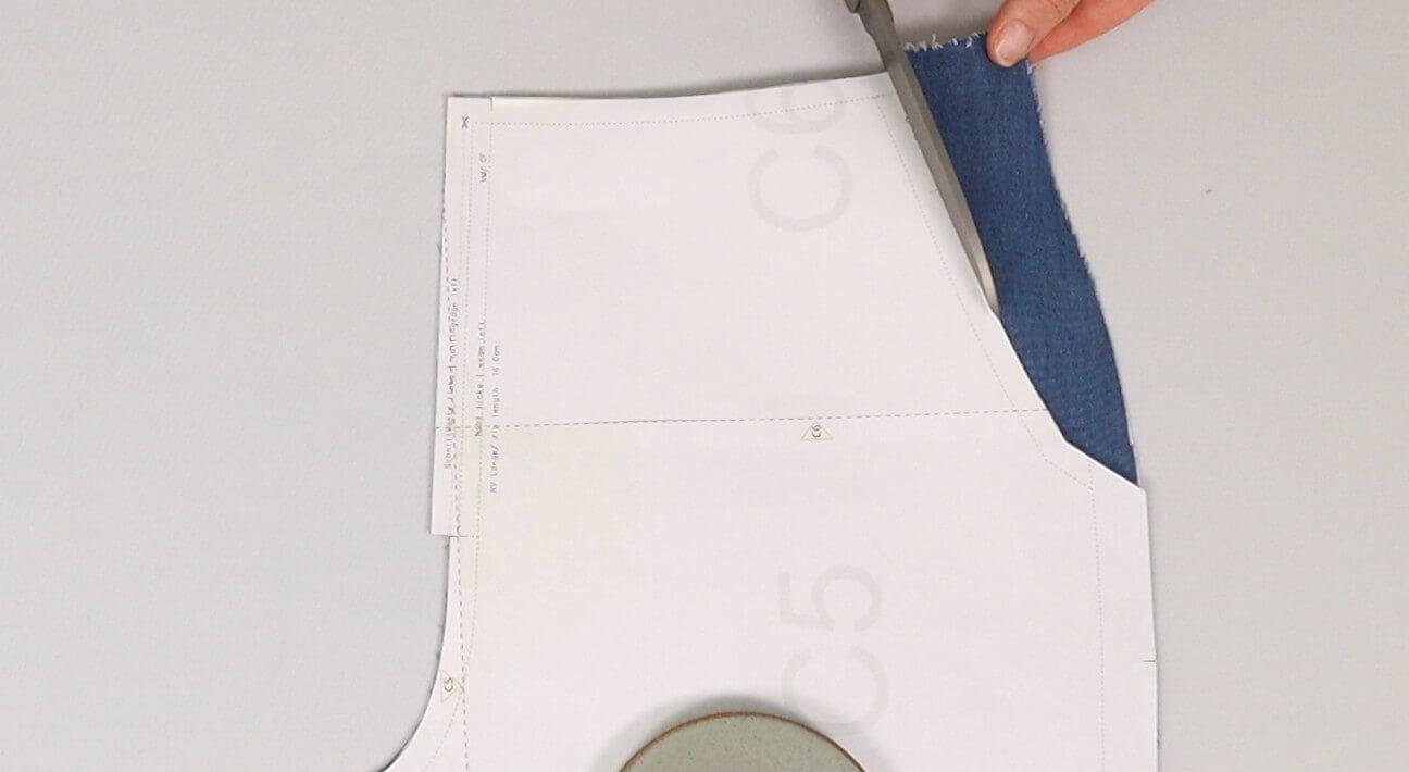 Das Bild zeigt, wie nach der Anprobe der Hose an den Vorderteilen die Tascheneingriffkanten am Schnittteil zurückgeschnitten werden.