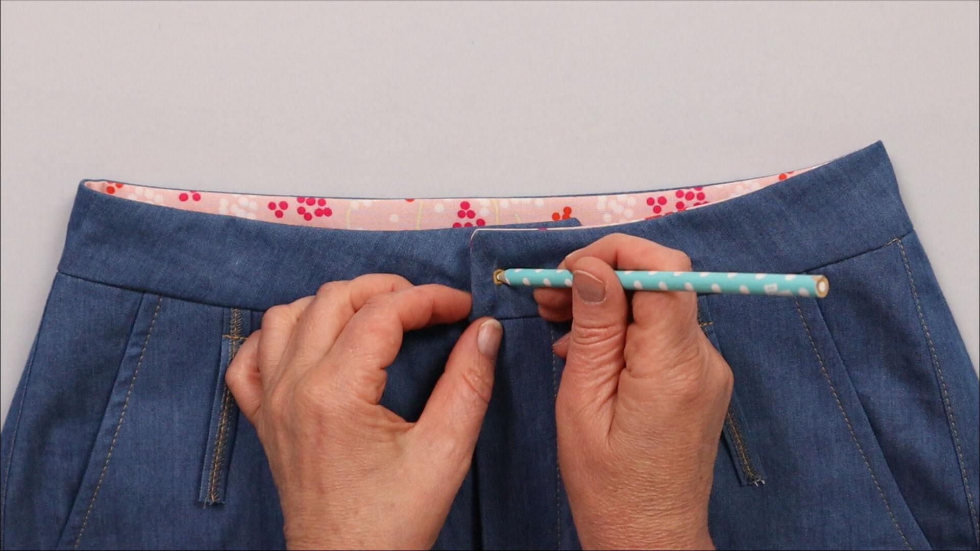 Das Bild zeigt, wie die Position des Knopfes auf dem Hosenbund markiert wird.