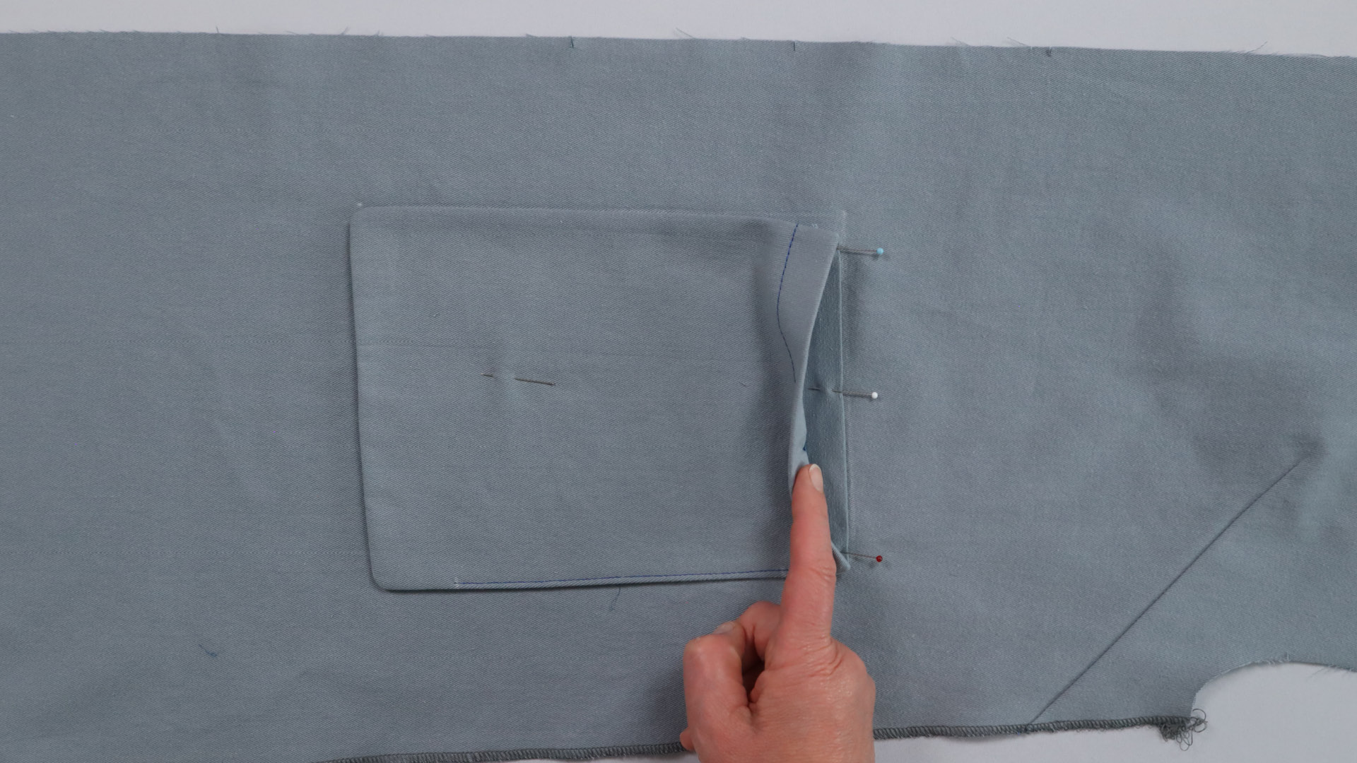 Parka mit Kapuze nähen - Die obere Kante des unteren Taschenbeutels wird festgesteckt.